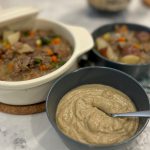 Hamburger soup with cream of mushroom. The soup is shown in a white tureen and a grey-blue bowl. Pureed hamburger soup is also shown in another bowl.